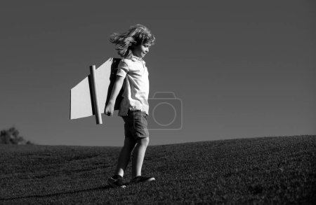 Porträt eines niedlichen blonden Kinderspielpiloten mit selbstgebastelten Flugzeugflügeln aus Papier. Kinderträume, Erfolg, kreatives und Startup-Konzept. Kopierraum für Text