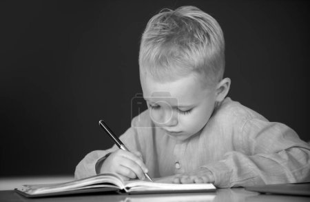 Photo for Little schoolboy study in a classroom at elementary school. Kid writing in notebook in class. Education and kids knowledge concept - Royalty Free Image