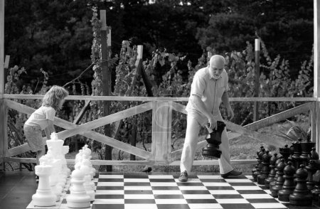 Téléchargez les photos : Grand-père et fils jouant aux échecs sur un grand échiquier. Week-end avec grand-père - en image libre de droit