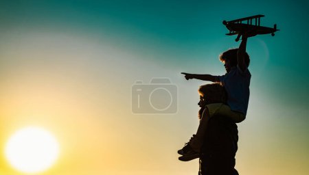 Photo for Success and child leader concept. Sunset silhouette of Father and son together. Boy child is sitting on daddy shoulder piggyback while the flight - Royalty Free Image