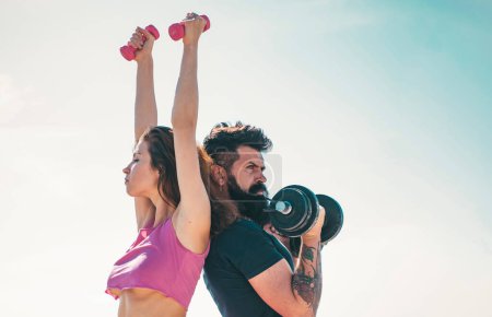 Photo for Fit sexy couple on sky background with dumbbells. Fitness concept. Sports couple training with dumbbell. Healthy coupl life style. Sporty woman in sexy pink sportswear - Royalty Free Image