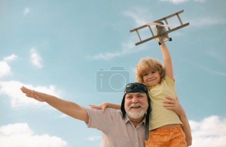 Téléchargez les photos : Grandfather and grandson having fun with plane outdoor on sky background with copy space. Child dreams of flying, happy childhood with granddad - en image libre de droit