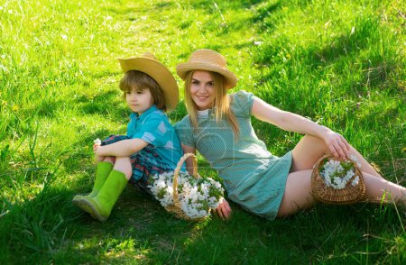 Glückliche Mutter am Frühlingstag mit Sohn beim Picknick. Familienmama mit Kind Junge sitzt auf dem Gras im Park mit Korb mit Blütenblüten