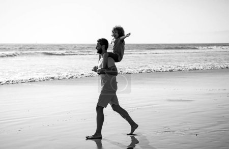 Téléchargez les photos : Père et fils marchent sur la mer. Beau père homme portant un jeune garçon fils. Joyeux papa tenant un enfant. Papa avec un gamin un jour d'été. Concept de famille amicale et de vacances d'été - en image libre de droit