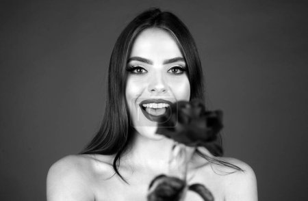 Photo for Portrait of a smiling woman with a rose flower. Beauty fashion model woman face. Portrait of a beautiful young girl with a red rose near face. Vogue spring summer style. No filter unaltered face - Royalty Free Image