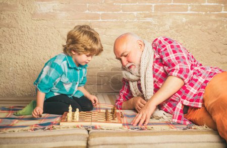 Téléchargez les photos : Homme mûr avec un petit garçon jouant aux échecs. Un échec mat. Joli petit garçon jouant aux échecs. Enfance. Concept de grand-père et petit-fils. Pièce d'échecs - en image libre de droit