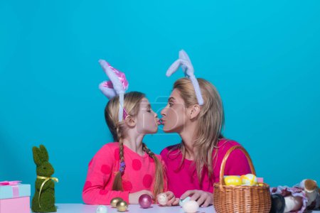 Téléchargez les photos : Vacances de Pâques. Une mère et sa fille peignent des œufs de Pâques, s'embrassent. Bonne famille se préparant pour Pâques, portant des oreilles de lapin de Pâques, portrait studio - en image libre de droit