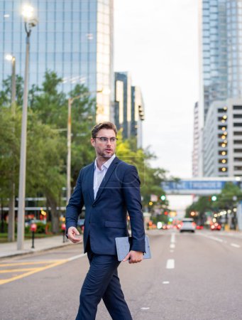 Foto de Hombre de negocios caminando por la calle en el centro de la ciudad moderna. Éxito empresarial del hombre de negocios al aire libre. Guapo empresario exitoso en traje elegante al aire libre - Imagen libre de derechos