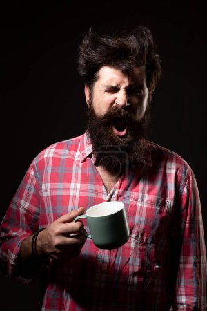 Photo for Mans holds cup of coffee and yawning on black. Morning tea. Yawning face. Man with tea cup. Hipster man yawning with cup of coffee. Bearded man yawning hold mug tea. Wake up. Happy day. After morning - Royalty Free Image
