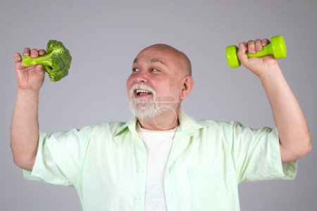 Photo for Healthy Senior. Healthy food. Power old mature man hold dumbbell and broccoli. Healthy old aged bearded gray haired mature man in studio. Healthy Vegan diet. Aged Dieting. Powerful health senior - Royalty Free Image