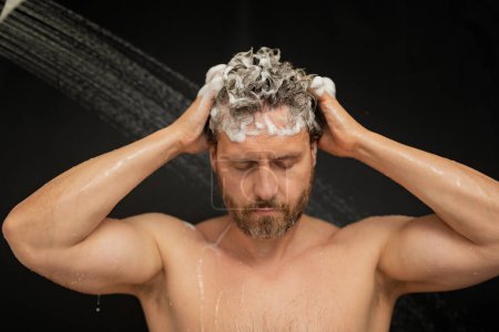 Téléchargez les photos : Homme lavant les cheveux dans le bain. Pommeau de douche dans la baignoire. Visage en mousse dans la douche. Un baigneur prend une douche. Gros plan gars douche. Concept de douche. L'homme est sous les gouttes d'eau dans les douches - en image libre de droit