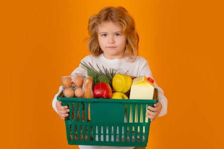 Téléchargez les photos : Un gamin au supermarché de légumes. Enfant avec panier. Enfant choisissant des aliments en magasin ou à l'épicerie - en image libre de droit