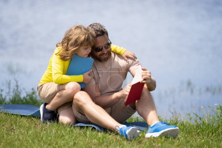Téléchargez les photos : Père et son fils lisent ensemble dans le parc d'été. Père et fils font un pique-nique dans le parc, concept de famille heureuse. Père et fils jouant au parc le jour. Famille amicale - en image libre de droit