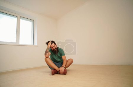 Téléchargez les photos : Un homme fatigué déménage chez lui. Déménagement dans un appartement vide - en image libre de droit