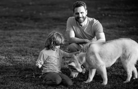 Téléchargez les photos : Père et fils avec chien de compagnie relaxant sur la nature dans le parc - en image libre de droit