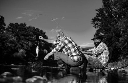 Photo for Catching fish. Young and old fisherman standing on the shore of lake with fishing rod. Father and son enjoy life. Men family, granddad and drandson fishing. Mature man fisher celebrate retirement - Royalty Free Image