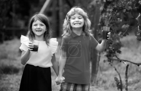 Foto de Dos niños beben batido verde al aire libre en el parque de verano. Hermano y hermana felices caminando en la naturaleza. Hermanos niño y niña jugando en el jardín - Imagen libre de derechos