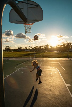Téléchargez les photos : Joyeux petit garçon jouant au basket sur une aire de jeux. mignon petit garçon enfant saut avec panier ballon pour coup - en image libre de droit