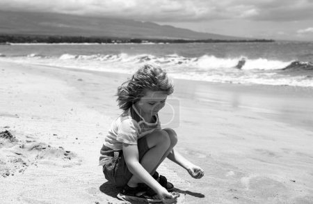 Photo for Cute boy playing with sand on summer tropical beach. Happy kid sit on the seaside sandy beach and playing with sand - Royalty Free Image