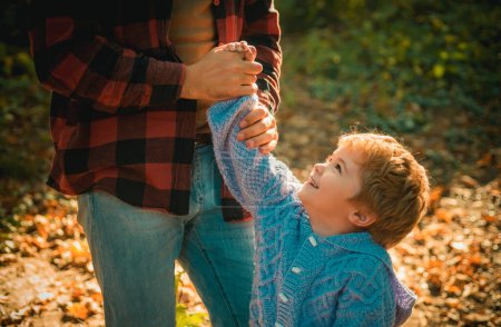 Foto de Strong father hand holding a little hand of his son walking down the forest on warm autumnal day. Little smiling toddler boy looking at his dad. Happy family and autumnal nature concept - Imagen libre de derechos