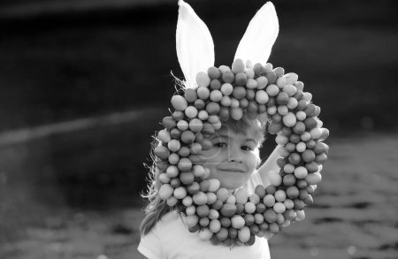 Foto de Niño con huevos de Pascua y orejas de conejo al aire libre. Lindo chico teniendo feliz Pascua en el parque. Niños divertidos cara de primer plano - Imagen libre de derechos
