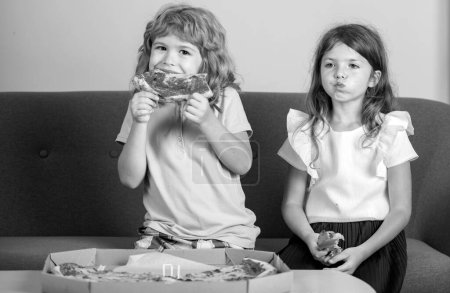Photo for Children eating pizza. Two young children bite pizza indoors - Royalty Free Image
