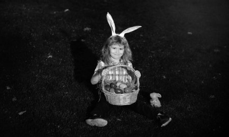 Foto de Niño lindo conejito con orejas de conejo. Huevos de Pascua en el jardín. Niño jugando en el campo, cazando huevos de Pascua - Imagen libre de derechos