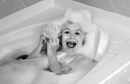 Foto de Niños bañándose. Un chico en una bañera. Lavado en el baño con jabón suds en el cabello. Niño tomando un baño. Retrato de primer plano del niño sonriente, cuidado de la salud e higiene infantil. Cara infantil en bañera con espuma - Imagen libre de derechos