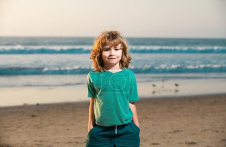 Téléchargez les photos : Mignon garçon enfant marchant sur la plage de la mer avec la main dans la poche - en image libre de droit