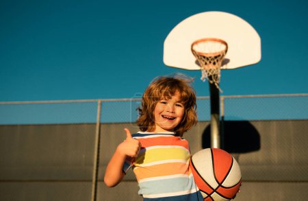 Foto de Lindo chico sonriente juega baloncesto. Niños activos disfrutando de juego al aire libre con pelota cesta. - Imagen libre de derechos