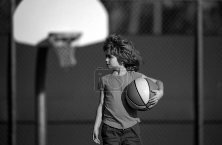 Foto de Lindo chico sonriente juega baloncesto. Niños activos disfrutando de juego al aire libre con pelota de cesta. Deporte para niños - Imagen libre de derechos