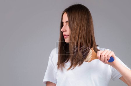 Young beautiful woman combing brown hair. Hair Care. Beautiful brunette woman hairbrushing hair with hairbrush. Brushing healthy hair with comb