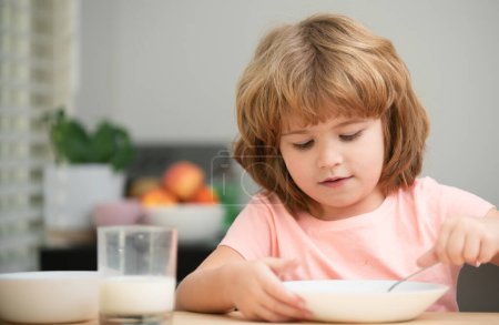 Téléchargez les photos : Un gamin drôle avec une assiette de soupe. Dîner enfant. Enfant d'âge préscolaire dégustant le petit déjeuner le matin, tenant cuillère - en image libre de droit