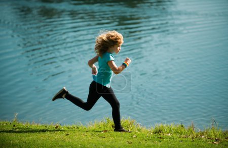 Téléchargez les photos : Enfants courir ou faire du jogging près du lac sur l'herbe dans le parc. Garçons jogging coureur dans le parc extérieur. Courir est un sport qui renforce le corps - en image libre de droit