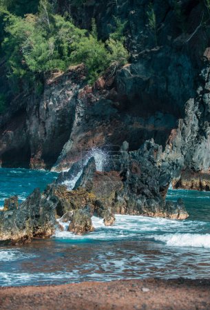 Téléchargez les photos : Belle plage océanique avec de grandes roches sur le rivage et dans l'eau. Des vagues dans l'océan. Vacances d'été, vacances. Plage de sable rouge, Maui en hawaïen - en image libre de droit