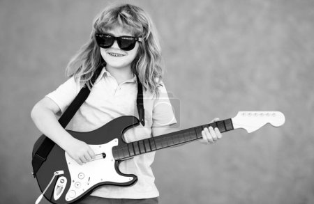 Téléchargez les photos : Boy with guitar. Child plays a guitar and sings, kids music and song. Funny little hipster musician child playing guitar - en image libre de droit