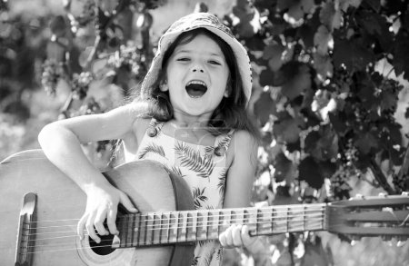 Téléchargez les photos : Enfant musicien excité jouant de la guitare comme une rockstar. Enfant souriant jouant à l'extérieur en été - en image libre de droit