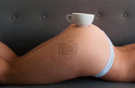 Foto de Sexy woman ass with cup of coffee in sofa. Sexy coffee. A cup of coffee on the bare female buttocks. Morning. Sexy morning. Coffee in bed. Coffe cup on womans sexy big ass - Imagen libre de derechos