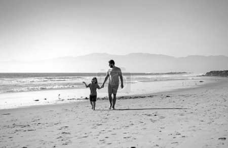 Foto de Papá y su hijo se divierten al aire libre. Padre e hijo caminando en la playa de verano. Papá y el niño tomados de la mano y caminando juntos - Imagen libre de derechos