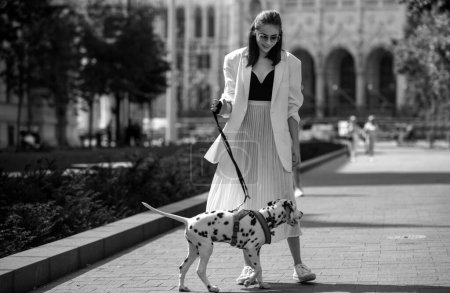 Téléchargez les photos : Portrait extérieur de jeune femme élégante marchant dans la rue. Jeune mannequin marchant avec chien, style urbain - en image libre de droit