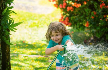 Foto de Niño adorable regando las plantas, desde el spray de manguera con manguera de agua en el jardín en el patio trasero de la casa en una noche de verano - Imagen libre de derechos