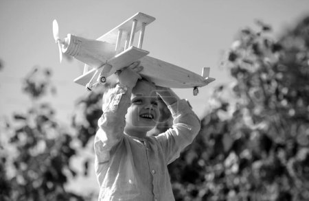 Foto de Sueños de vuelo. Niño jugando con avión de juguete contra el cielo. Sueños de viajes. Un niño soñando con un avión de juguete juega al aire libre. Niño rubio, cara de emoción sonriente - Imagen libre de derechos