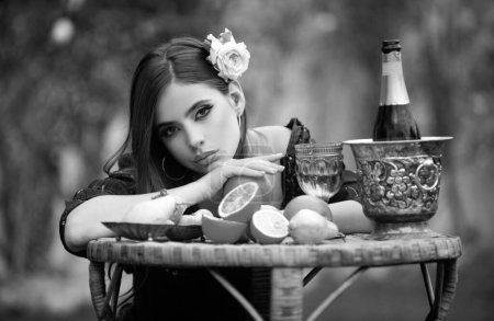 Foto de Retrato de chica sexy en el picnic de verano en una hierba en el parque con vino y frutas frescas. Foto de moda al aire libre de la hermosa mujer joven con rosa en el pelo. Belleza mujer cara - Imagen libre de derechos