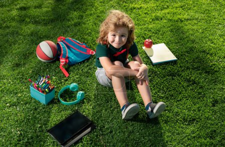 Téléchargez les photos : Enfant assis sur l'herbe avec tablette dans le parc. École de plein air - en image libre de droit