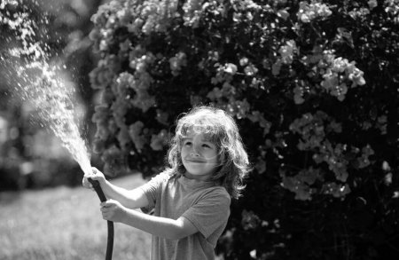 Téléchargez les photos : L'enfant arrose la plante à l'extérieur de la maison, concept d'activité d'apprentissage de la culture végétale pour les enfants et éducation des enfants à la nature - en image libre de droit