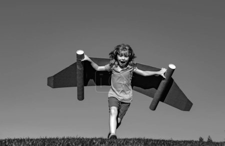 Téléchargez les photos : Joyeux enfant jouant avec jetpack jouet. Pilote enfant s'amusant sur l'herbe verte en plein air. Succès, innovation des enfants et concept de leader - en image libre de droit