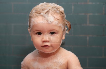 Téléchargez les photos : Bain bébé. Enfant heureux avec de la mousse de savon sur la tête. Les enfants drôles font face de près. Bain d'enfant dans la baignoire - en image libre de droit