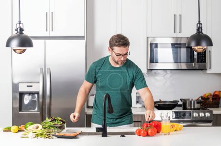 Porträt eines gutaussehenden Mannes in der Küche. Junger Mann bereitet in der heimischen Küche leckeres und gesundes Essen zu. Mann mit Rezept kocht Gemüsesalat in der Küche. Lebensmittel Gemüse bereit zum Kochen. Gesunde Ernährung