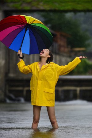 Rainy day. Funny excited woman in raincoat hold umbrella with rainy water drops. Girl in rain coat under falling water drops in rainy season. Woman with umbrella. Summer rain. Rainy weather
