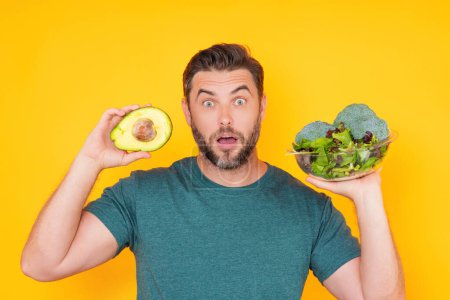 Photo for Man hold avocado, isolated on yellow. Man holding avocado and broccoli vegetables. Cooking avocado. Dieting, bowl with salad. Green avocado. Healthy vegan food concept. Fresh vegetables - Royalty Free Image